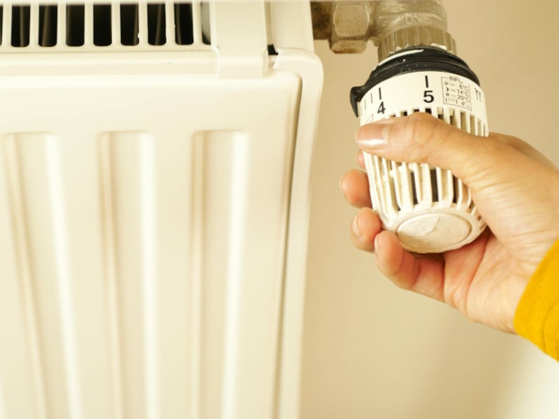 Hand turning a thermostatic valve on a radiator