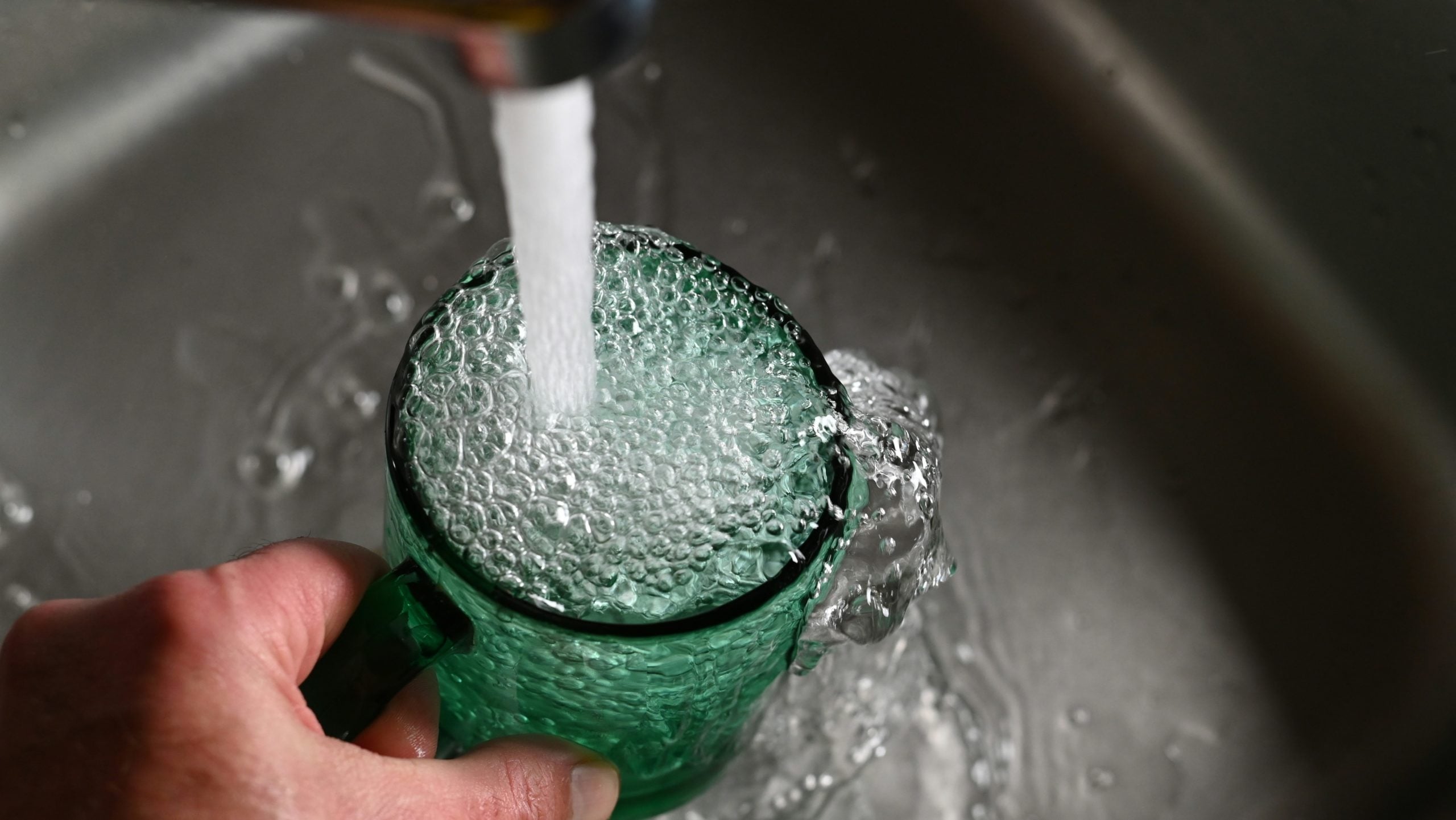 A hand holding a green glass, filling up with water from an overhead tap