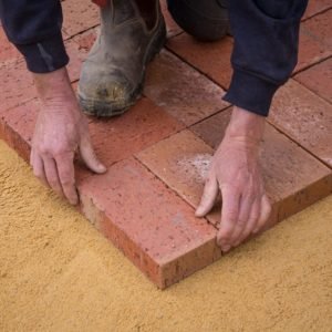 Man laying block paving on sand base