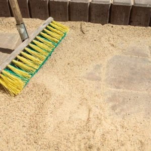 Wooden handle brush on sand next to paving slabs with joints filled in with sand