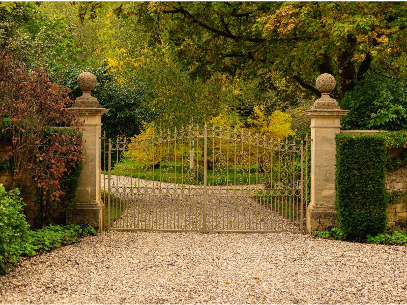 Gravel driveway leading from an iron gate with stone pillars either side in a traditional style