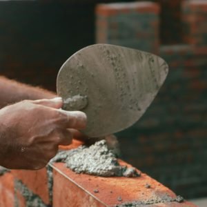 Mortar being applied to a red brick wall with a trowel