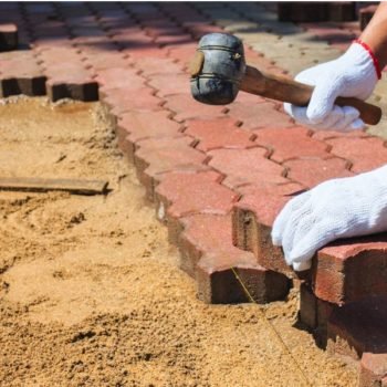 Worker wearing white gloves holding rubber mallet placing blocks on sand