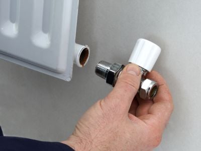 person holding a radiator lockshield valve next to a radiator