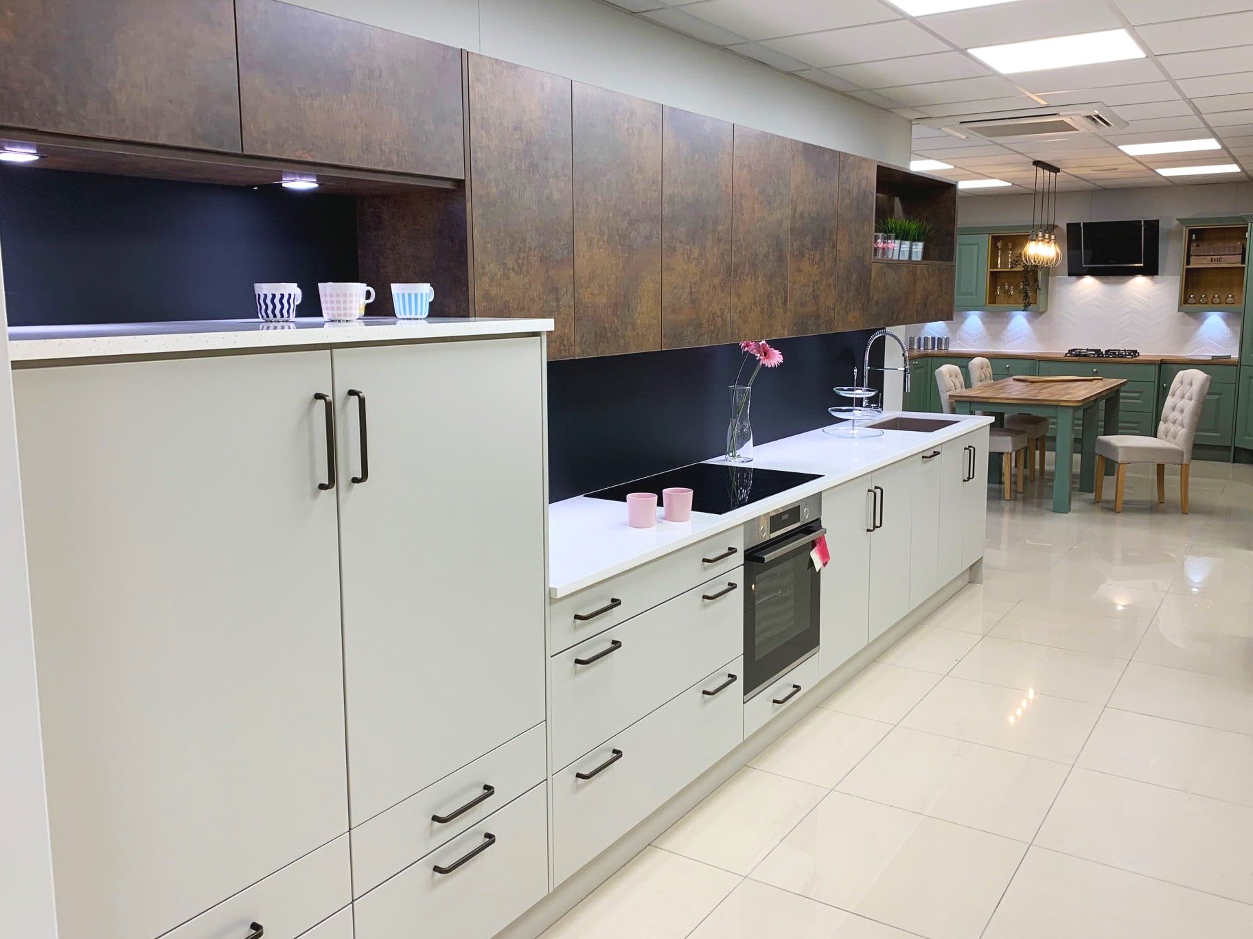 (foreground) Rotpunkt matt kitchen with copper effect units (background) Sheraton Shaker traditional kitchen in Green